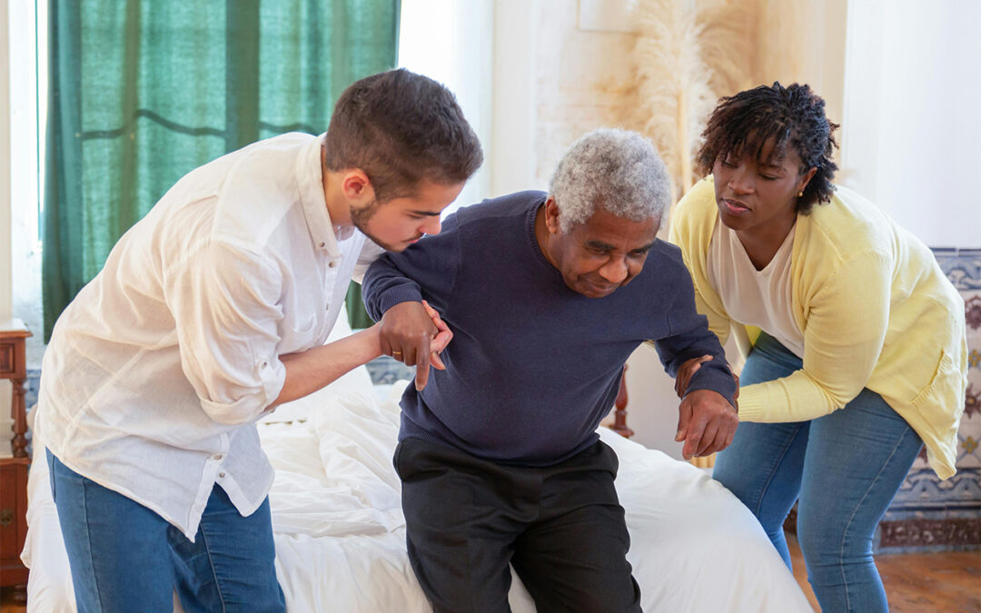 Caregivers assisting an elderly man to stand