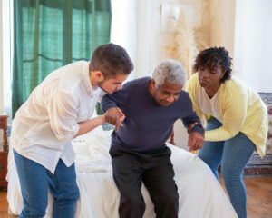 Caregivers assisting an elderly man to stand